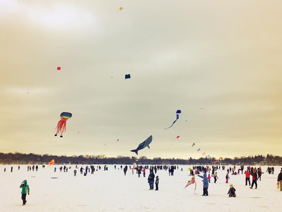 People standing on ice and flying colorful kites at Lake Harriet Kite Festival. 