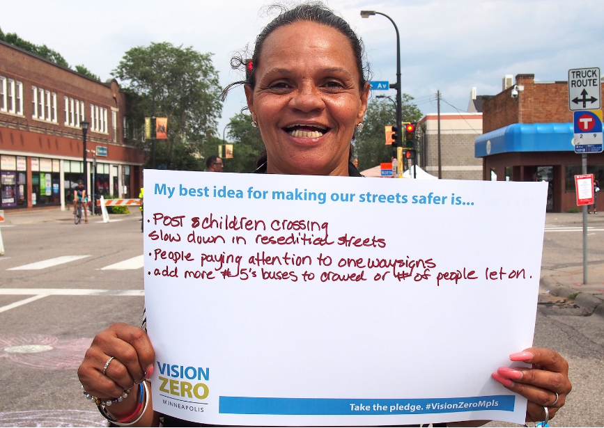 Person holding sign "My best idea for making streets safer: post children crossing, slow down on residential streets, pay attention to 1 way signs..."