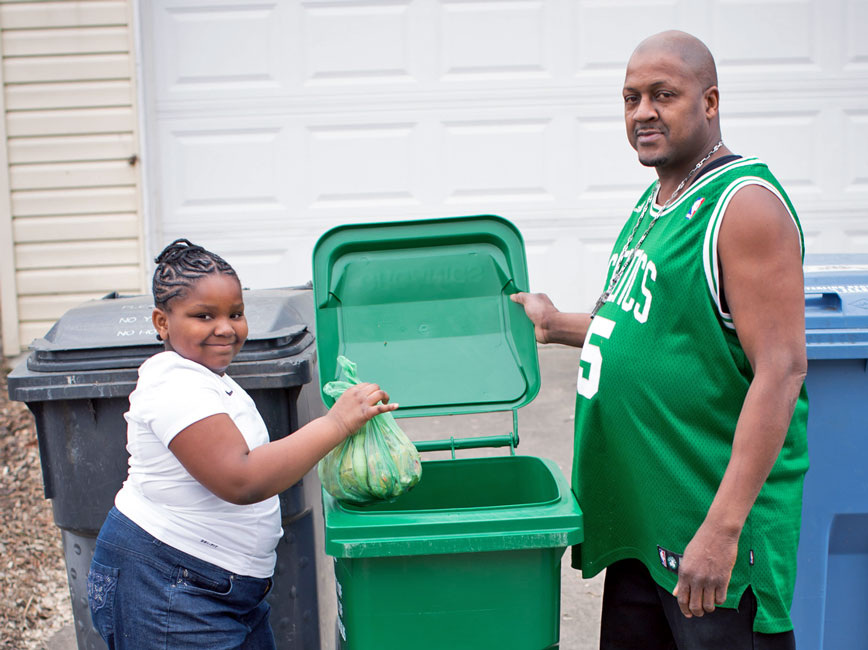 Dad and daughter put compost items into organics recycling bin.