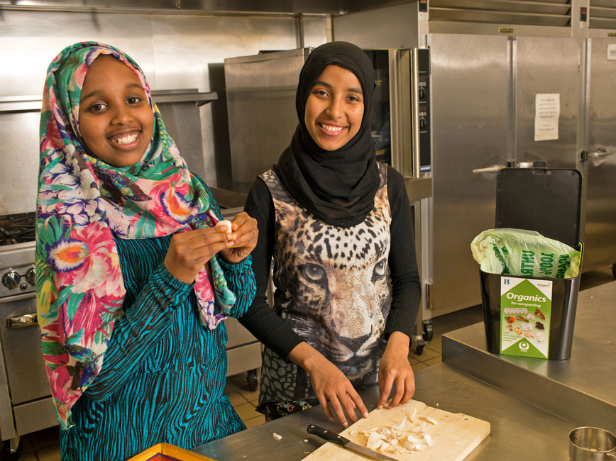 two girls in kitchen sorting food scraps while preparing a meal