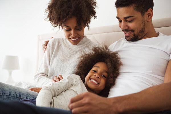 Two adults looking lovingly at smiling child on their lap.
