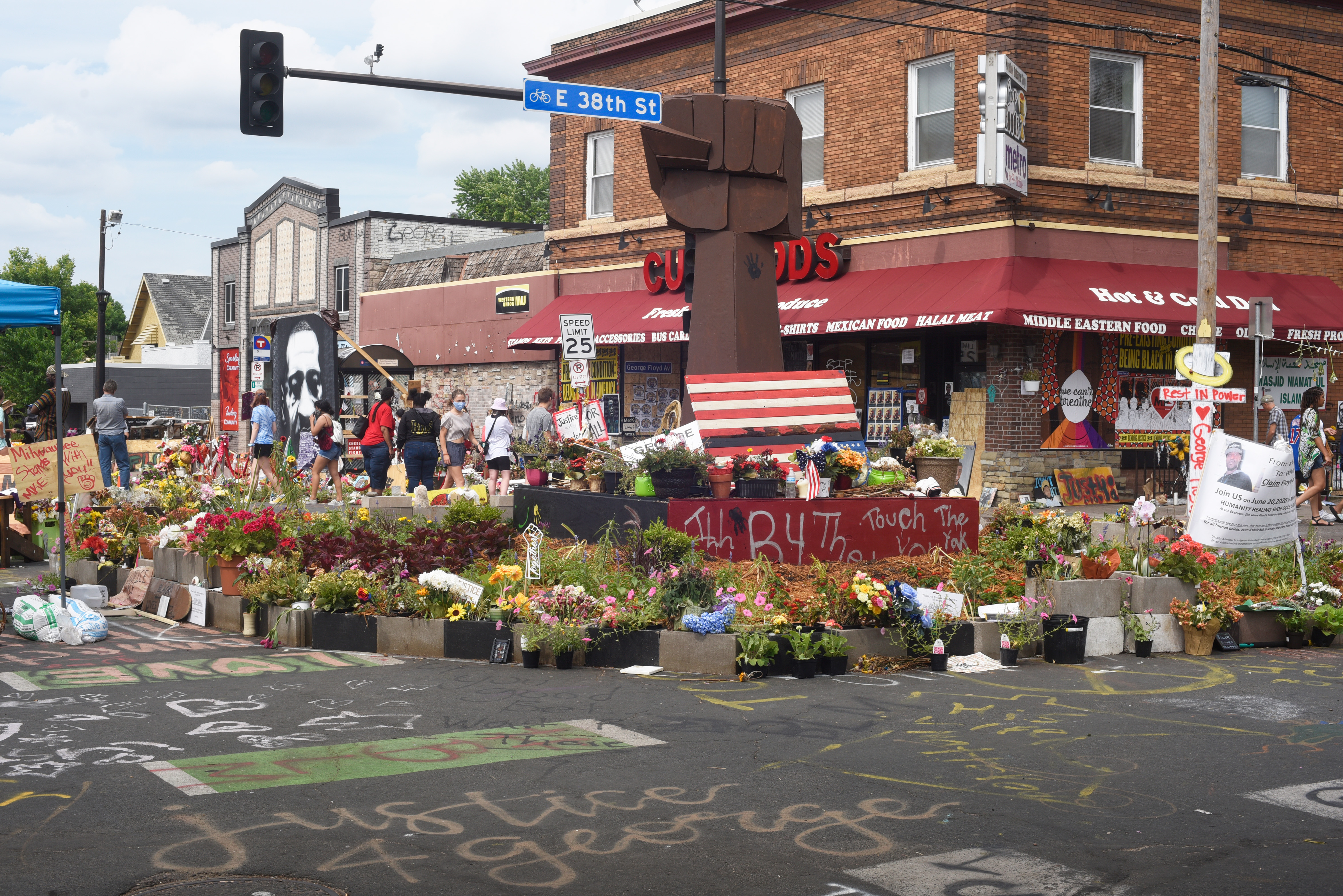 Wooden raised‑fist sculpture surrounded by flowers at George Floyd Square memorial.