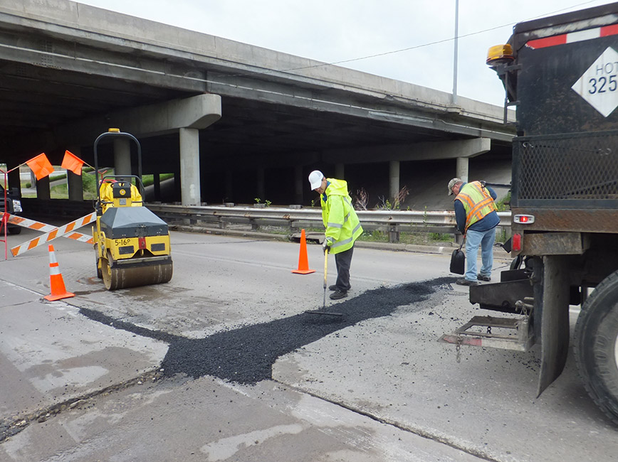 A crew fills a pothole in a road. A crew fills a pothole in a road.