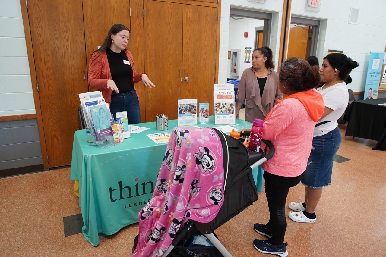 People behind a table covered by a green tablecloth, talking to visitors