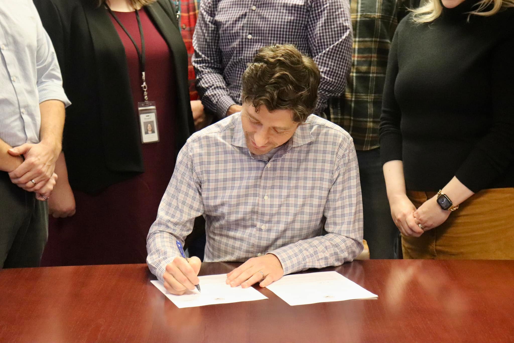 Mayor Frey signing a document with people standing behind me.