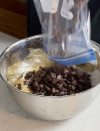 Bowl of cookie dough with chocolate chips being poured in.