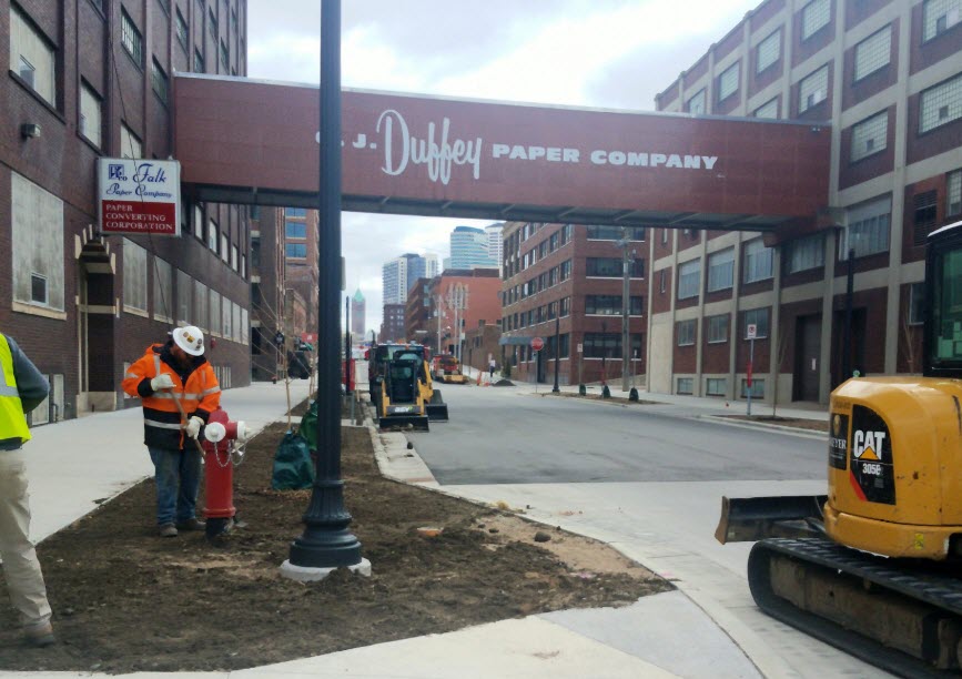Concrete sidewalk, dirt boulevard, and paved street with construction equipment