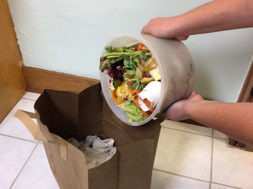 A pail of organics being dumped into a brown paper grocery bag
