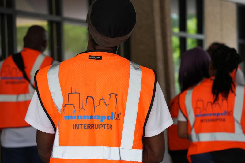 The back of a violence interrupter who is wearing a bright orange vest
