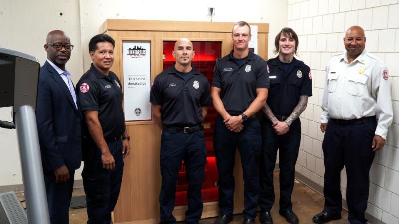 A group of firefighters and city leadership pose in front of a donated sauna.