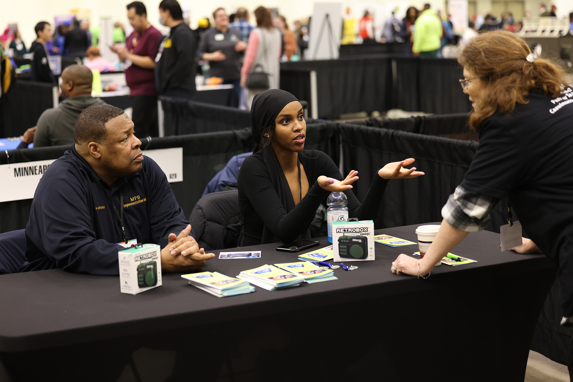 Two members of the MPD Implementation Unit talk to a community member while tabling at a community engagement event.