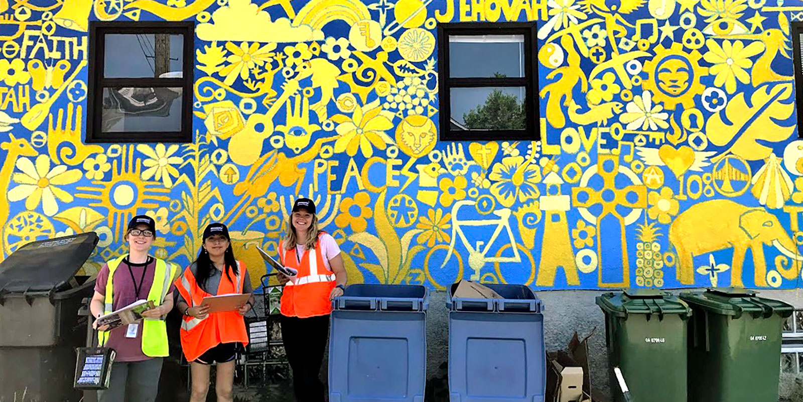 City interns standing by mural and recycling containers