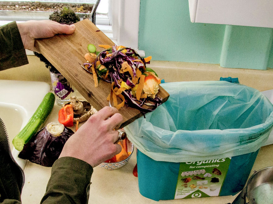 person scraping food scraps into a kitchen pail off a cutting board