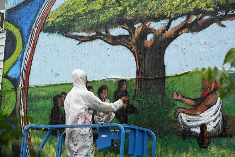 person in white jumpsuit painting a mural