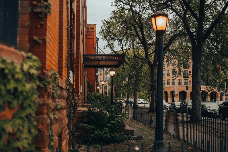 Street Lamp Near Brown Brick Building with a fence, sidewalk and cars parked along the street.
