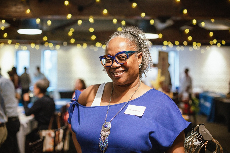 Person in a room with others in the background and lights hung. 