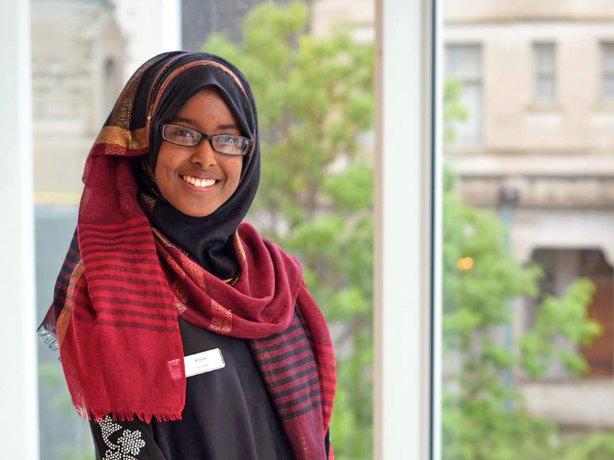Smiling young person wearing glasses and colorful garments standing by window. Smiling young person wearing glasses and colorful garments standing by window.