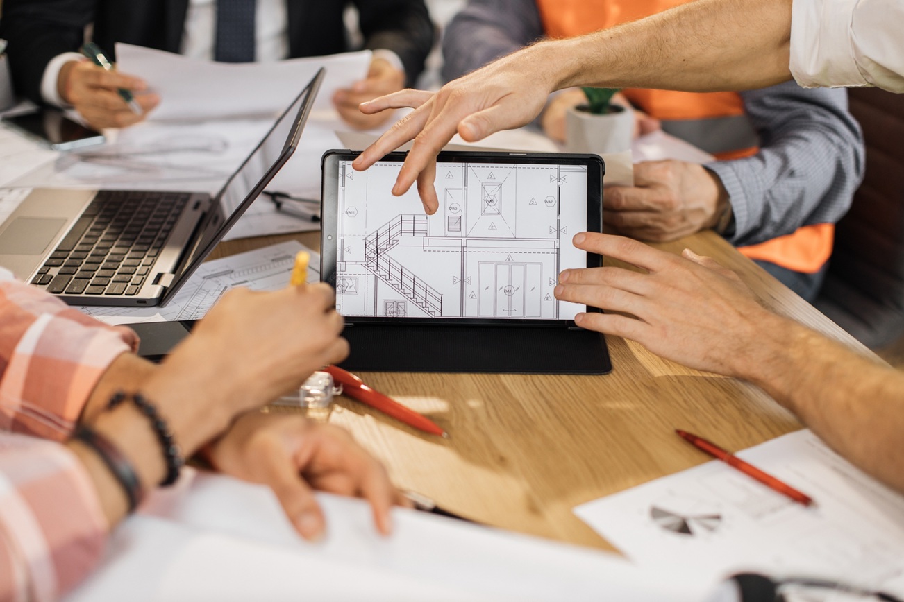 Many hands reviewing blueprints on a tablet