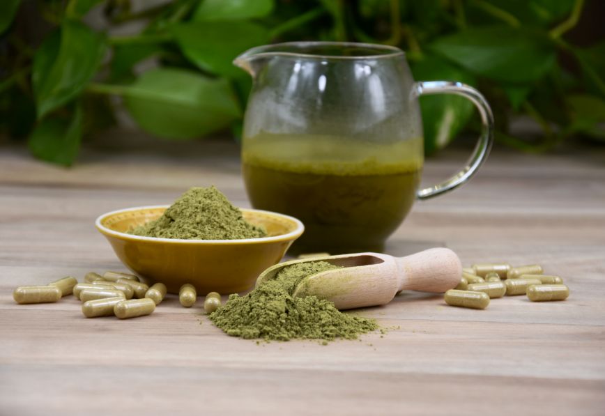 Green kratom beverage in a glass mug with green kratom powder and green kratom capsules